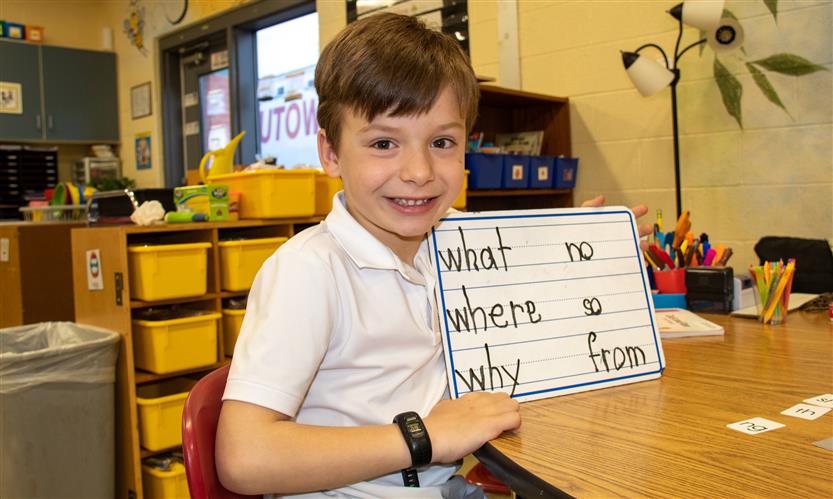 A boy with brown hair holds a dry erase board.